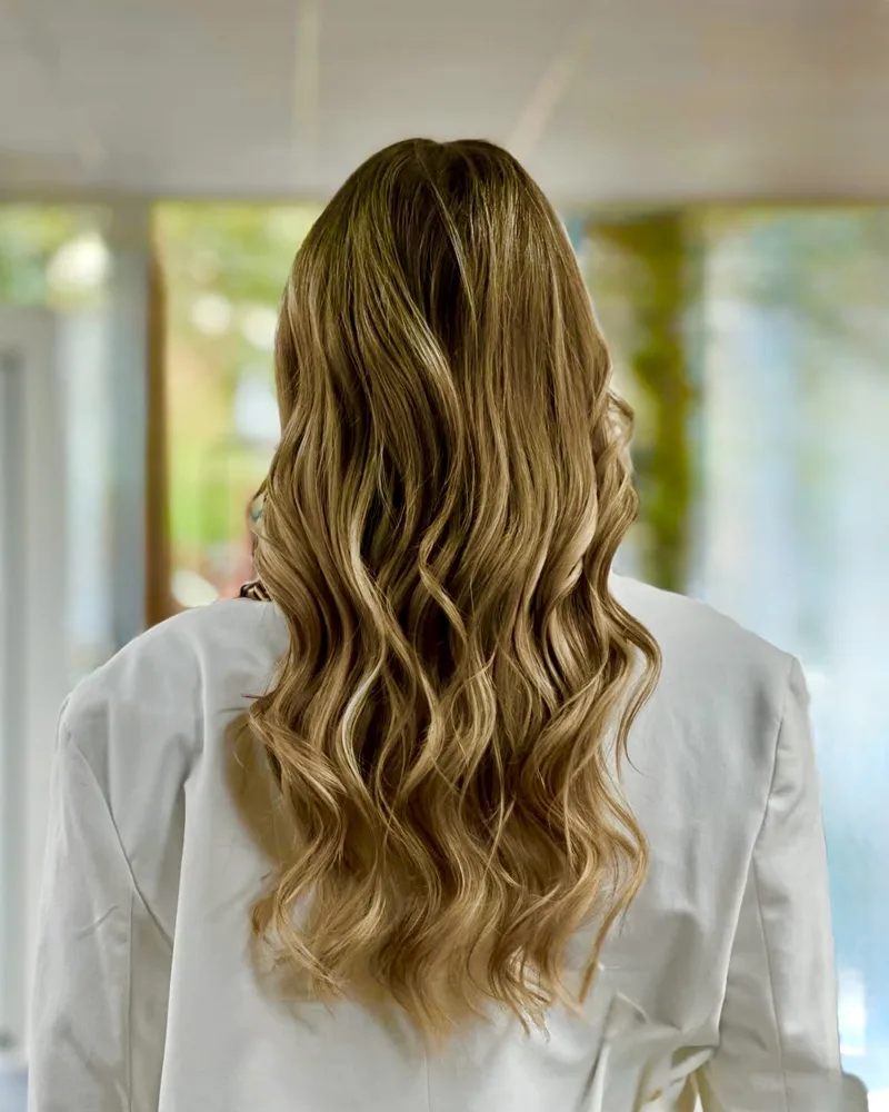 Long blonde balayage styled in loose waves, seen from behind